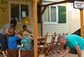 Familia disfrutando comida y barbacoa en la terraza de madera de SunLodge Maple en Marina di Venezia, Italia.