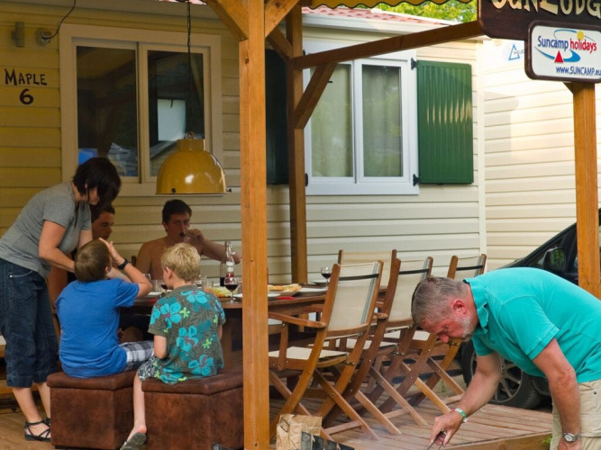 Familia disfrutando comida y barbacoa en la terraza de madera de SunLodge Maple en Marina di Venezia, Italia.