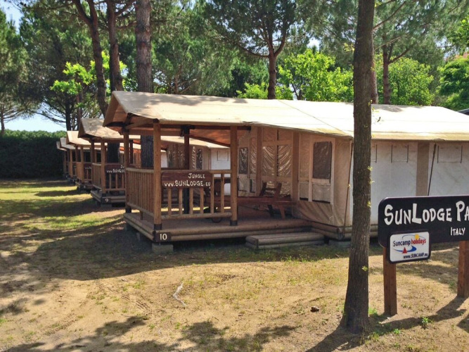 Fila de tiendas SunLodge Jungle en Camping Union Lido Mare, Italia, rodeadas de árboles y sombra.