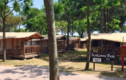 La soleada SunLodge Jungle en Camping Union Lido Mare, Italia, rodeada de árboles y cabañas de madera.