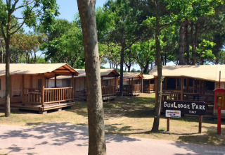 La soleada SunLodge Jungle en Camping Union Lido Mare, Italia, rodeada de árboles y cabañas de madera.
