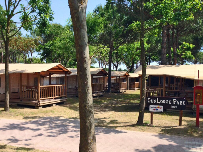 La soleada SunLodge Jungle en Camping Union Lido Mare, Italia, rodeada de árboles y cabañas de madera.