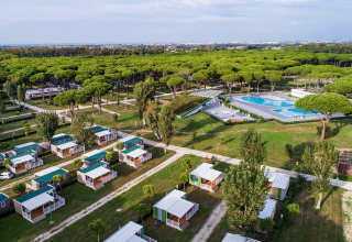 Vista aérea de un lodge con pequeñas cabañas, zonas verdes, un bosque y una gran piscina al aire libre.