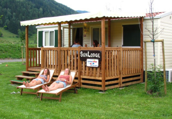 Two women relaxing on loungers outside SunLodge Maple, a wooden porch lodge surrounded by lush greenery.