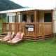 Two women relaxing on loungers outside SunLodge Maple, a wooden porch lodge surrounded by lush greenery.