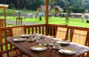 Outdoor dining area at SunLodge Maple, set table on wooden deck overlooking lawn, tents, and distant hills.