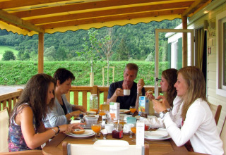 Cinco personas desayunan juntas en la terraza de SunLodge Maple, rodeados de colinas verdes.