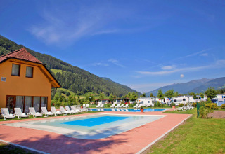 Piscina exterior en SunLodge Maple, rodeada de tumbonas, montañas verdes y caravanas bajo el sol brillante.