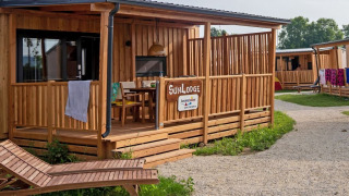Buitenzicht op SunLodge BigLeaf bij Camping Terme Catez in Slovenië, met houten veranda en ligstoelen.