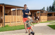 Un hombre y un niño juegan al fútbol frente a cabañas de madera en SunLodge BigLeaf durante el día.