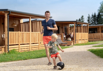 Un hombre y un niño juegan al fútbol frente a cabañas de madera en SunLodge BigLeaf durante el día.