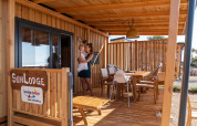 Donna con bambino in braccio sulla terrazza in legno della SunLodge BigLeaf, tra mobili da esterno.