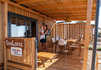 Donna con bambino in braccio sulla terrazza in legno della SunLodge BigLeaf, tra mobili da esterno.
