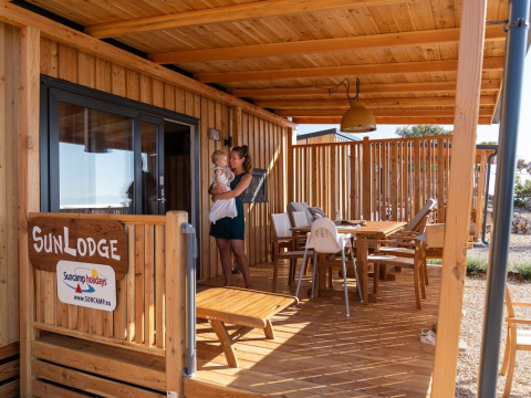 Mujer con un niño en brazos en la terraza de madera de SunLodge BigLeaf, con muebles de exterior.