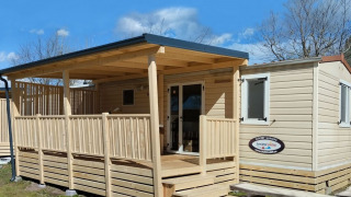 Een luxe houten lodge met overdekt terras en trap, ideaal voor een zonnige en ontspannen vakantie.