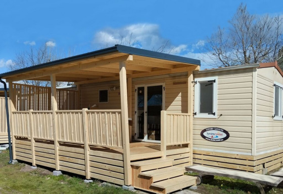 Un lodge de luxe en bois avec terrasse couverte et escalier, idéal pour un séjour détente au soleil.