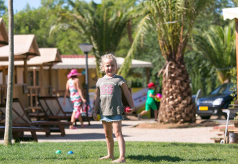 Bambina che gioca sull’erba davanti a una tenda safari SunLodge Jungle al Camping Vilanova Park in Spagna.