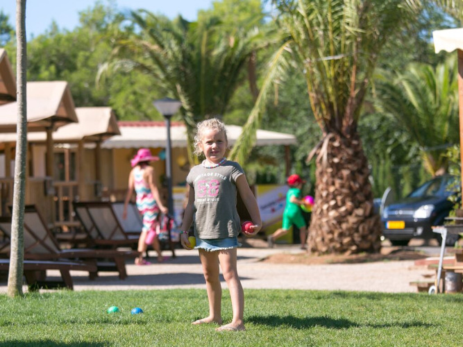 Niña juega en el césped delante de una tienda safari SunLodge Jungle en el Camping Vilanova Park en España.