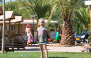 Child playing on grass in front of a SunLodge Jungle safari tent at Camping Vilanova Park in Spain.