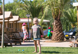 Niña juega en el césped delante de una tienda safari SunLodge Jungle en el Camping Vilanova Park en España.