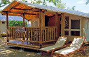 Safari tent SunLodge Jungle with a wooden porch and loungers at Camping Vilanova Park in Spain, shaded by trees.