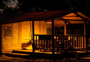 Tenda safari illuminata SunLodge Jungle di notte con veranda e biciclette a Camping Vilanova Park, Spagna.