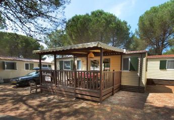 SunLodge Aspen met overdekte houten veranda en buitenzitplaats, omgeven door hoge dennenbomen.