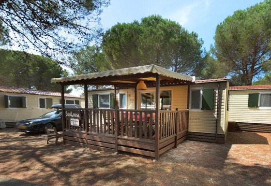 SunLodge Aspen con terraza de madera cubierta y asientos exteriores, rodeada de altos pinos verdes.