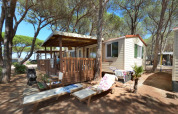 Cabaña SunLodge Aspen en Camping Village Baia Blu La Tortuga, Italia, rodeada de pinos y bancos de madera.