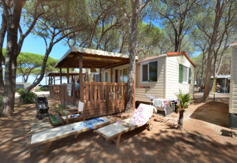 SunLodge Aspen cabin at Camping Village Baia Blu La Tortuga, Italy, surrounded by pine trees and benches.