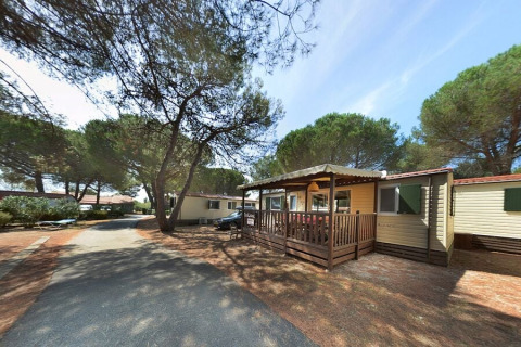 SunLodge Aspen hytte ved Camping Village Baia Blu La Tortuga i Italien, omgivet af fyrretræer.