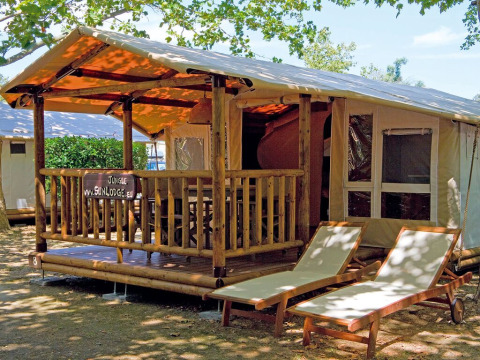 SunLodge Safari met houten terras en ligstoelen op Camping Village Cavallino in Italië, midden in het groen.