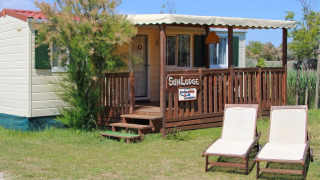 Sunny image of SunLodge Maple with two lounge chairs on grass in front of a cozy wooden porch.