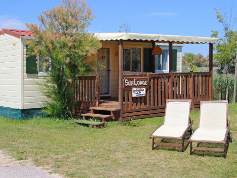 Sunny image of SunLodge Maple with two lounge chairs on grass in front of a cozy wooden porch.