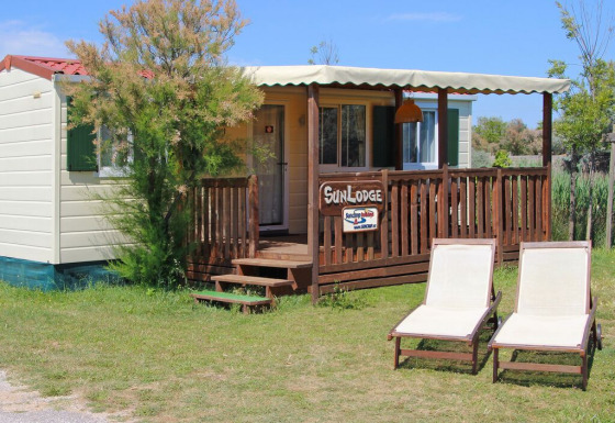 Sunny image of SunLodge Maple with two lounge chairs on grass in front of a cozy wooden porch.
