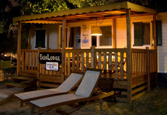 Vista nocturna de SunLodge Maple en Camping Leï Suves, Francia, con terraza iluminada y tumbonas afuera.