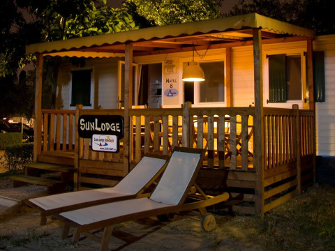 Vista nocturna de SunLodge Maple en Camping Leï Suves, Francia, con terraza iluminada y tumbonas afuera.