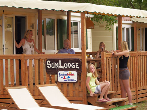 En familie hygger sig på verandaen af SunLodge Maple ved Camping Leï Suves (Suncamp) i Frankrig.