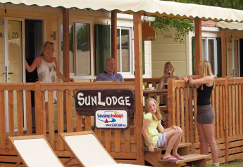 Gezin ontspant op de veranda van SunLodge Maple bij Camping Leï Suves (Suncamp) in Frankrijk, bord zichtbaar.