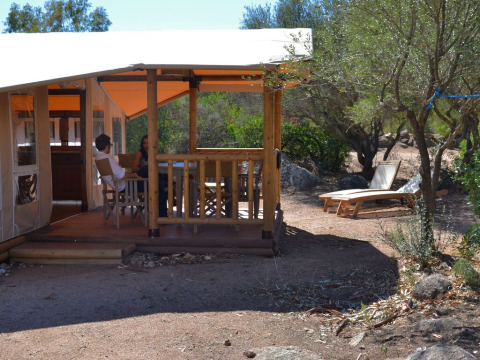 Twee personen zitten op het terras van een SunLodge Safari bij Centro Vacanze Isuledda, Italië, omringd door bomen.