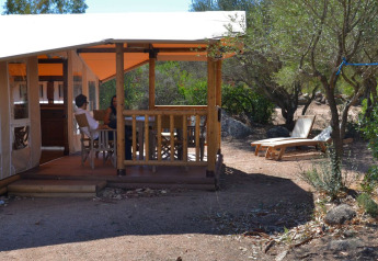 Twee personen zitten op het terras van een SunLodge Safari bij Centro Vacanze Isuledda, Italië, omringd door bomen.