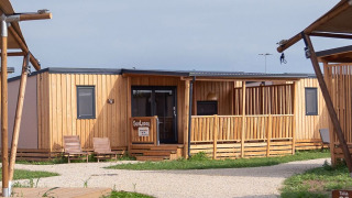 Foto van SunLodge Catalpa, een moderne houten lodge met terras en ligstoelen te midden van het groen.