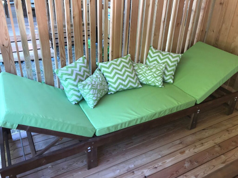 Green lounge chair with patterned pillows on a wooden deck at SunLodge Catalpa, Camping Cisano/San Vito, Italy.