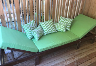 Tumbona verde con cojines estampados sobre tarima de madera en SunLodge Catalpa, Camping Cisano/San Vito, Italia.