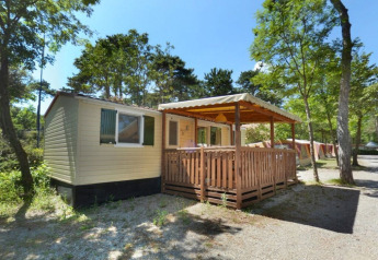 SunLodge Aspen bij Camping Village Mare Pineta in Italië, met houten terras en omgeven door bomen.