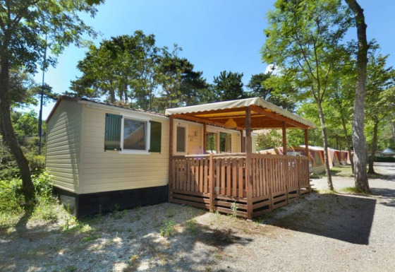 SunLodge Aspen bij Camping Village Mare Pineta in Italië, met houten terras en omgeven door bomen.