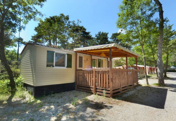 SunLodge Aspen en Camping Village Mare Pineta, Italia, con terraza cubierta y rodeada de árboles.