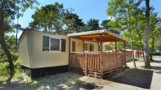 SunLodge Aspen en Camping Village Mare Pineta, Italia, con terraza cubierta y rodeada de árboles.