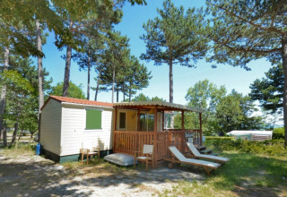 SunLodge Aspen en Camping Village Mare Pineta, Italia, con terraza, tumbonas y rodeado de altos pinos.