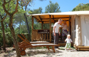 Famille profitant du soleil devant la tente SunLodge Safari au Camping Leï Suves, entourée de nature en France.